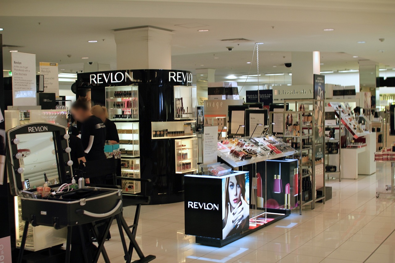 Sisätiloissa kosmetiikkamyymälä, Revlon-esittelypiste, meikkituotteita ja valaistu näyttö, asiakkaat taustalla.
Matkailijoille on runsaasti ostoskohteita Suomessa.