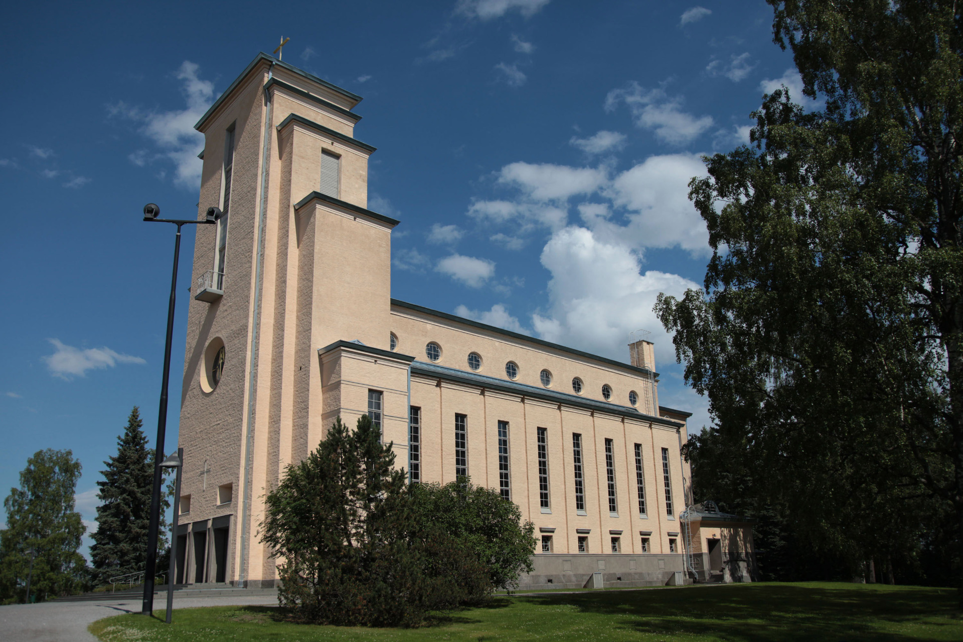 Tiilirakennuksen kirkontorni ja pitkät ikkunarivit, taustalla sininen taivas ja puut. Taulumäen kirkko. Jyväskylä.