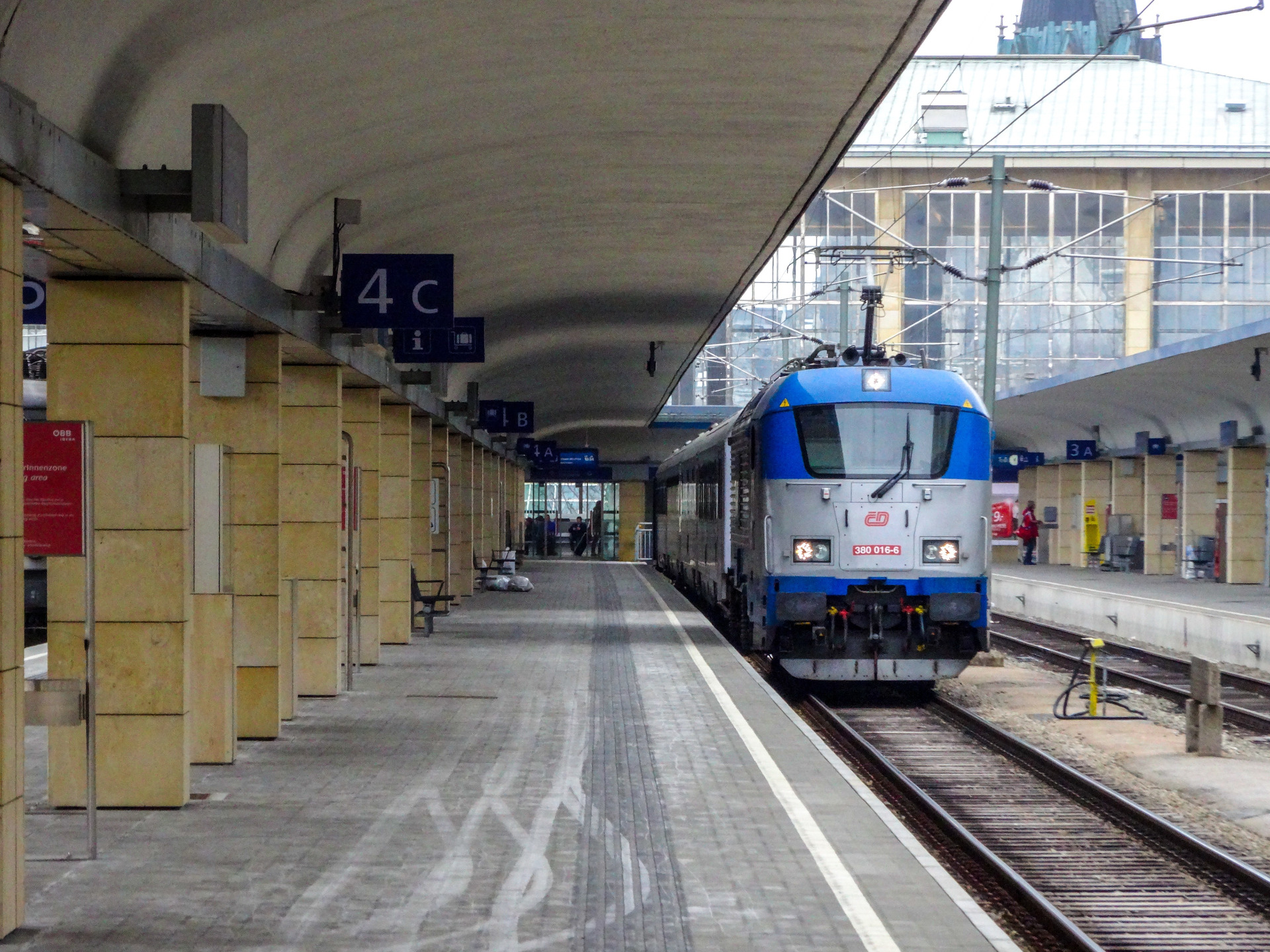 Sininen ja valkoinen sähköjuna odottaa laiturilla, katos, opasteet ja kiskot näkyvät. Julkinen liikenne Itävallassa toimii erittäin hyvin. Wien. Rautatieasema, Itävalta