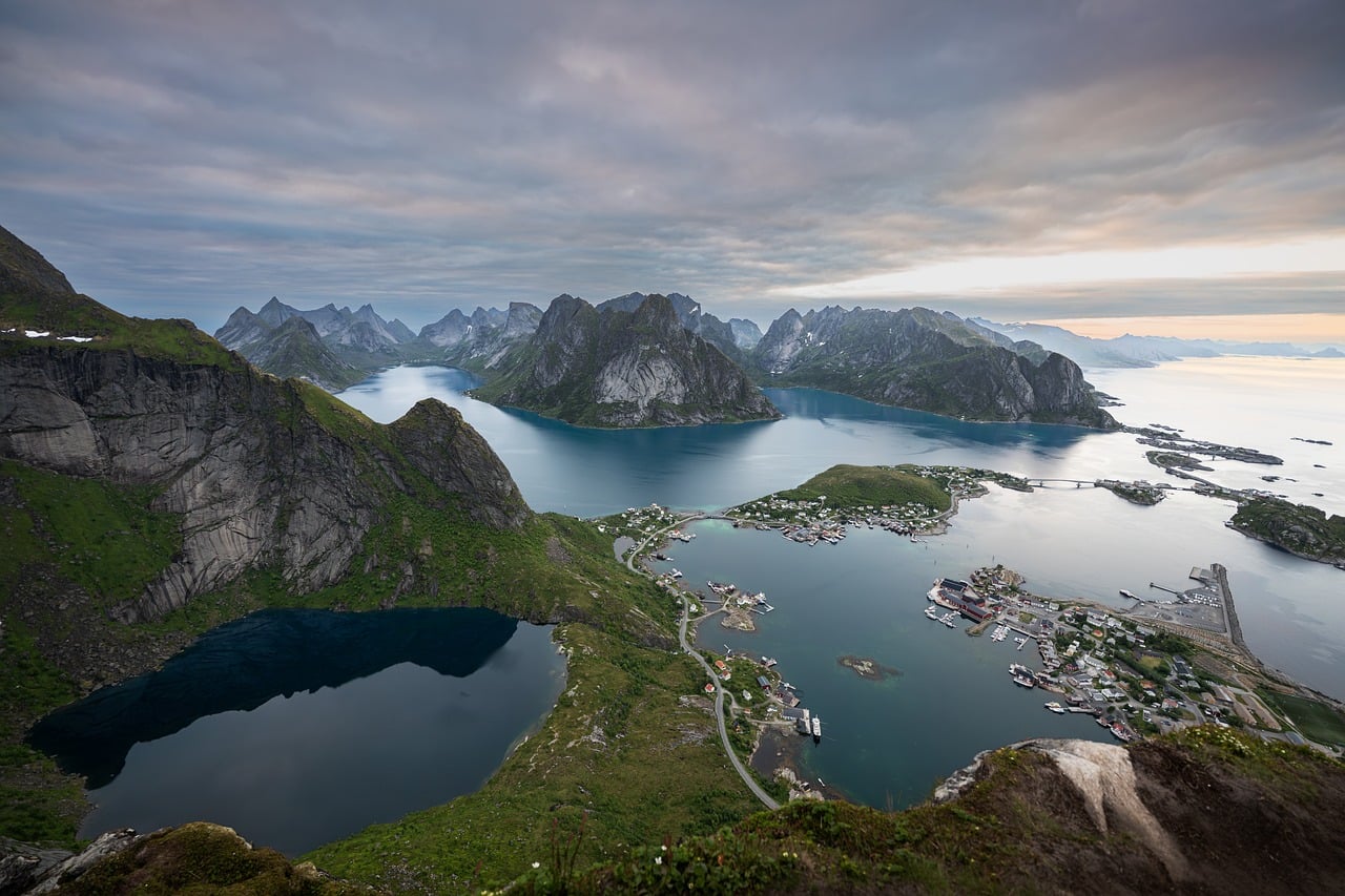 Lofootit, Norway. Reinebringen. Vuoristoinen rannikko, sininen vuono ja satama, näkymä vihreiltä rinteiltä kohti kaukaisia saaria.