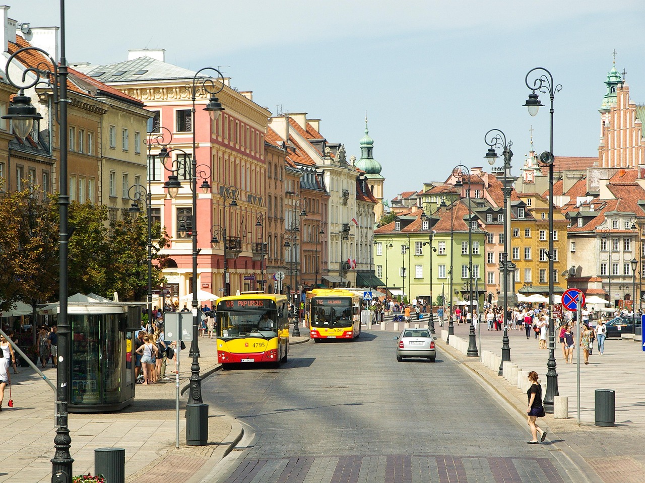 Varsova on vilkas matkailukaupunki. Kaupunkinäkymä Puolan vanhankaupungin kadulta, raitiovaunuja, busseja, liikennemerkit ja kirkontorni taustalla.