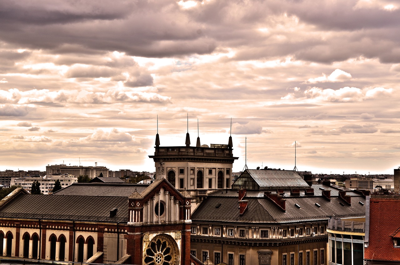 Bucarest, Romania on vilkas ja eläväinen suurkaupunki. Kaupungin kattoja ja historiallinen rakennus, taustalla pilvinen taivas ja auringonvaloa pilvien raoista.