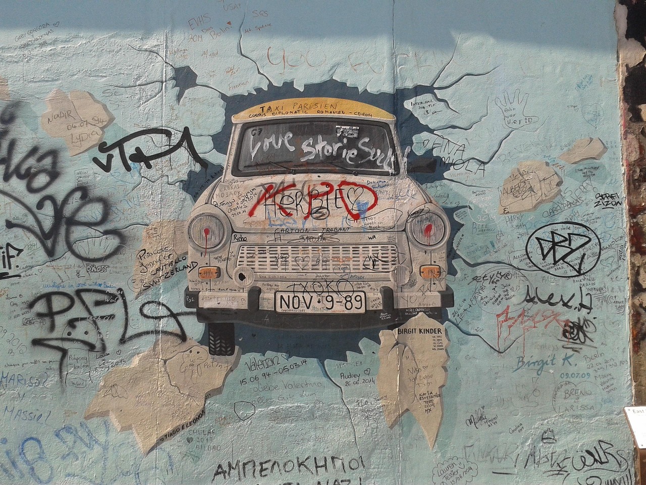 Saksan historia pitää myös autoteollisuutta sisällään. Trabant oli suositti Itä-saksalainen kansanauto. Graffitien peittämä seinä, keskellä vanha taksi, jossa teksti “True Stories” ja päivämäärä “NOV 19-89”.