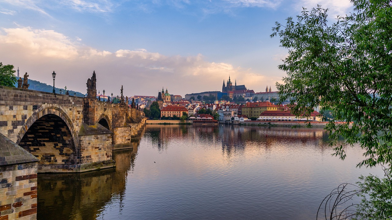 Kaarlen silta ja Praha ovat lomailijoiden suosikkeja. Kivinen silta ja joki, taustalla Prahan vanhakaupunki, kirkontornit ja punaiset katot iltataivaalla.
