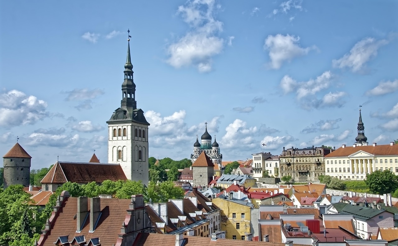 Tallinna, vanhakaupunki, Virossa on suomalaisten suosima matkakohde. Historiallinen kaupunkimaisema, kirkontorneja ja punakattoisia taloja sinisellä taivaalla, pilviä taustalla.