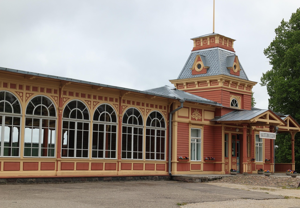 Haapsalu on kesäkaupunki, Länsi-Virossa. Haapsalun asema on vanha historiallinen rakennus, kaarevat ikkunat ja harmaa katto, edessä museo-kyltit ja pihapolku.
