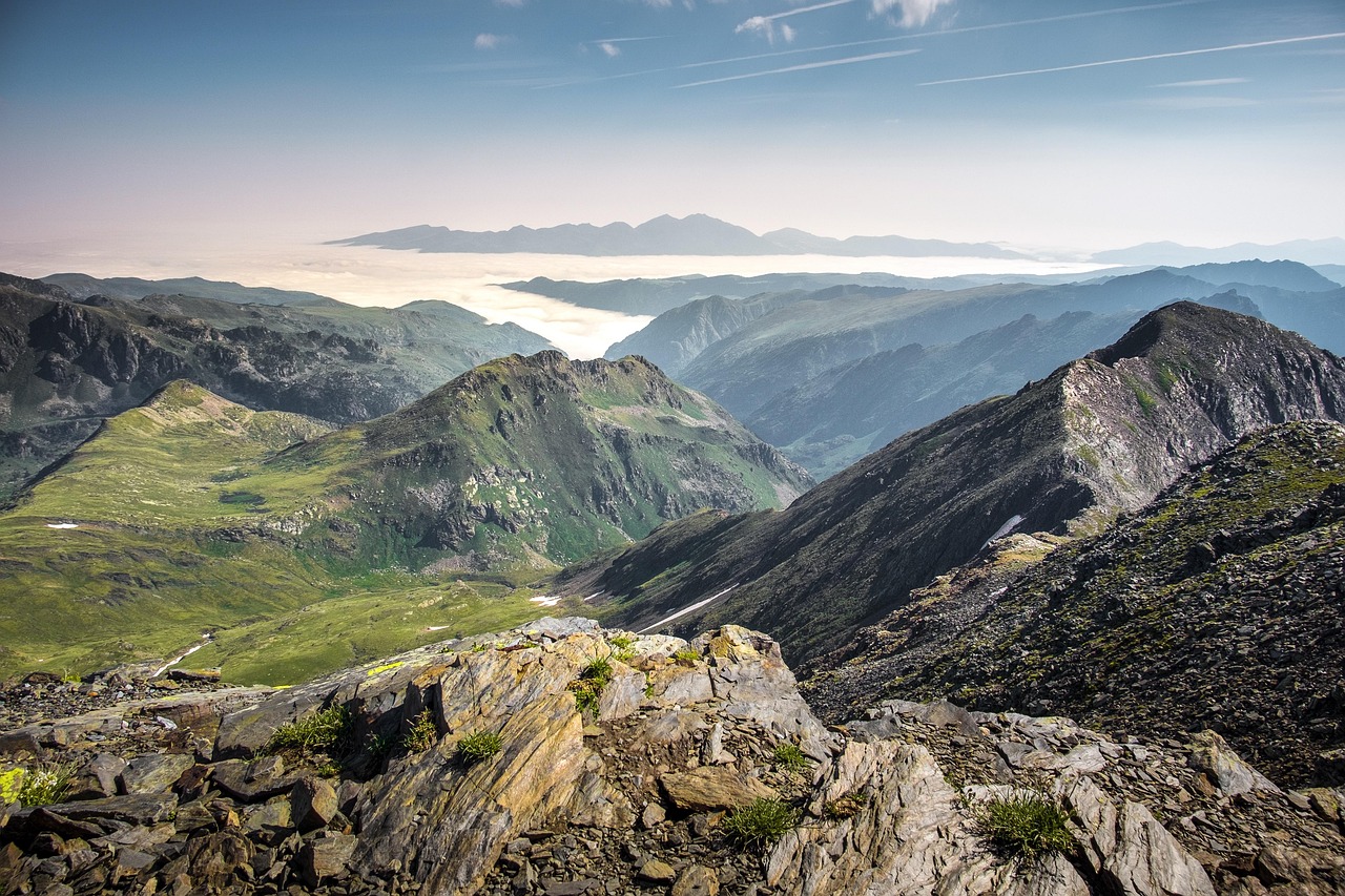 Andorra. Pyreneiden vuoristoa Espanjan ja Ranskan välissä. Vuoristomaisema, vihreitä rinteitä ja kivikkoisia huippuja, laaksojen sumua ja kaukaisia harjanteita sinisellä taivaalla.