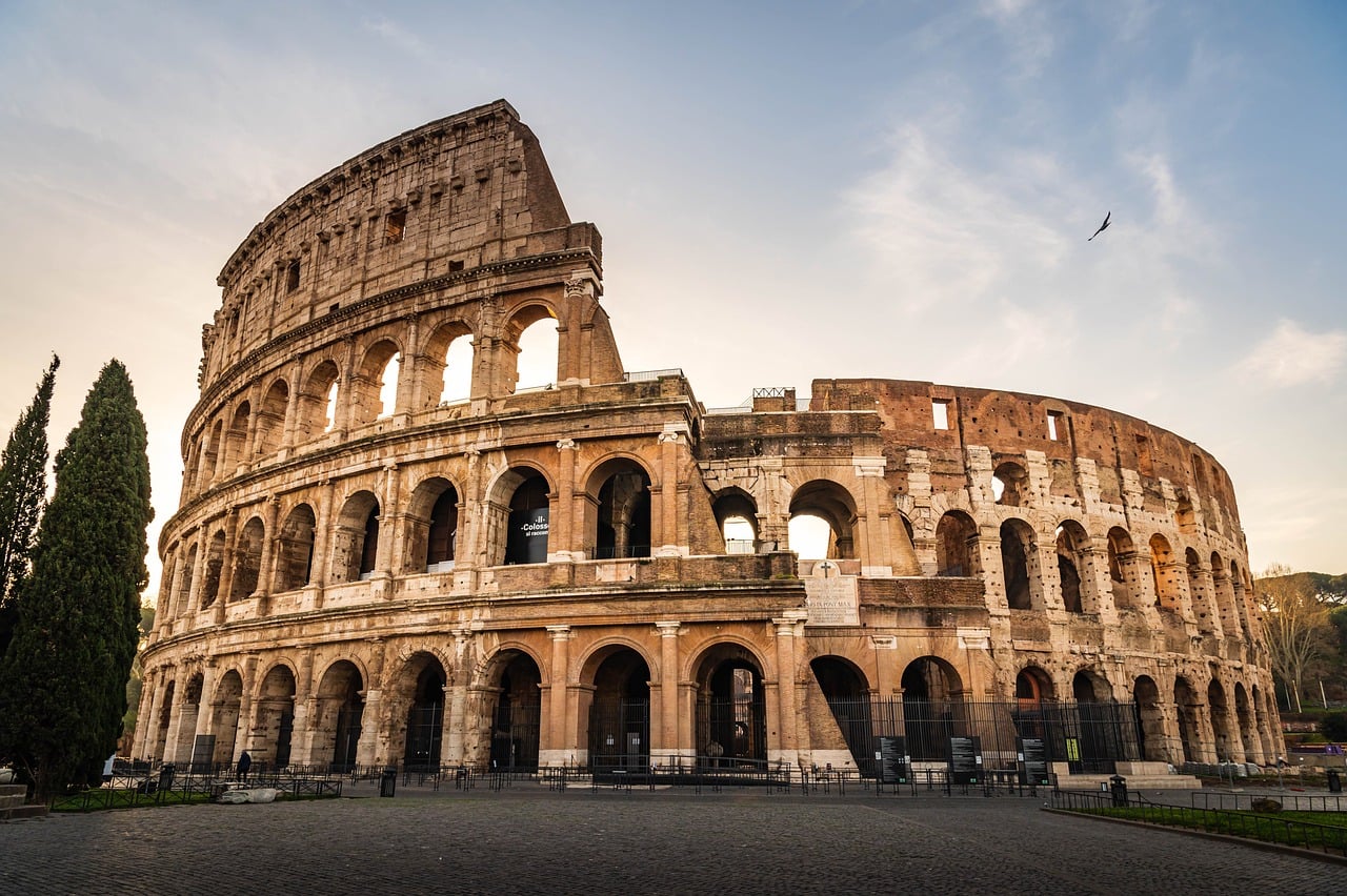 Colosseum, muinainen kivinen amfiteatteri Roomassa, kaarevia holveja ja kaareva katto taivasta vasten.