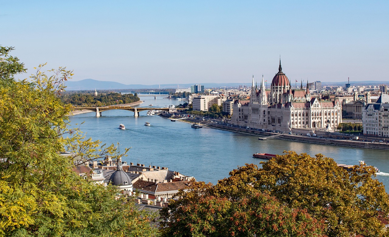 Budapest sijaitsee Tonavan varrella Unkarissa.
Tonavirta ja silta, näkymä Budapestin parlamenttirakennukseen ja kaupunkimaisemaan puiden lomasta.