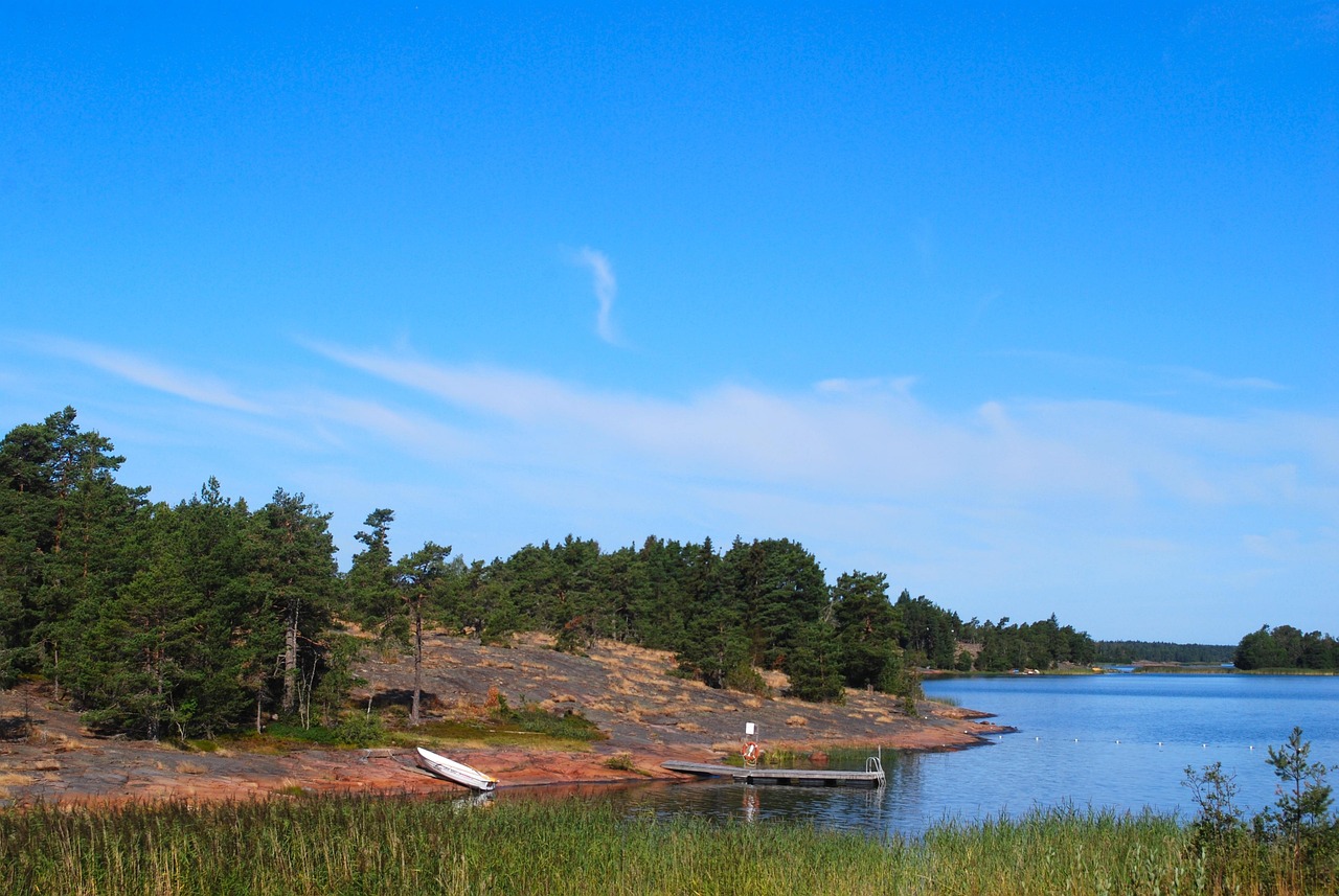 Vårdössa kohtaat kauniin saaristoluonnon.
Metsäinen rantaviiva, pieni vene laiturilla ja sininen järvi kirkkaalla taivaalla.