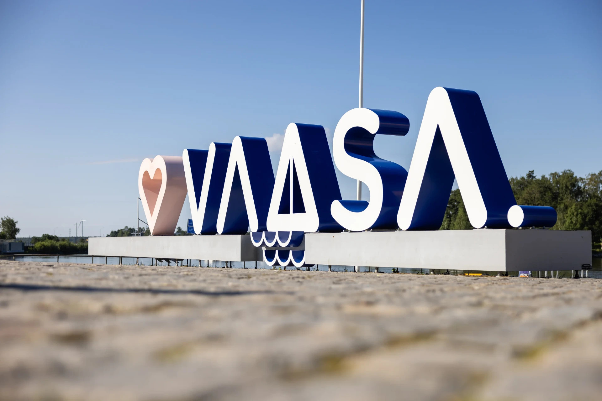 Vaasan kaupunki on kesäisin matkailijan unelmakohde.
Sininen ja valkoinen jättimäinen WANSA-logo ulkomainoksessa taivasta vasten, etualalla betoninen reunus.