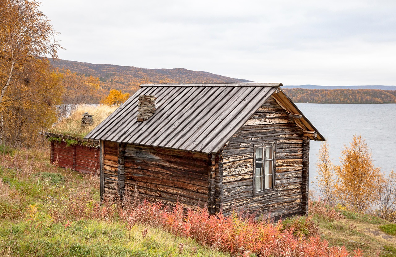 Utsjoki tarjoaa luonnon kauneutta, karuutta ja hiljaisuutta.
Hylätty hirsinen mökki järven rannalla, syksyiset puut ja kukkivat pensaat taustalla.