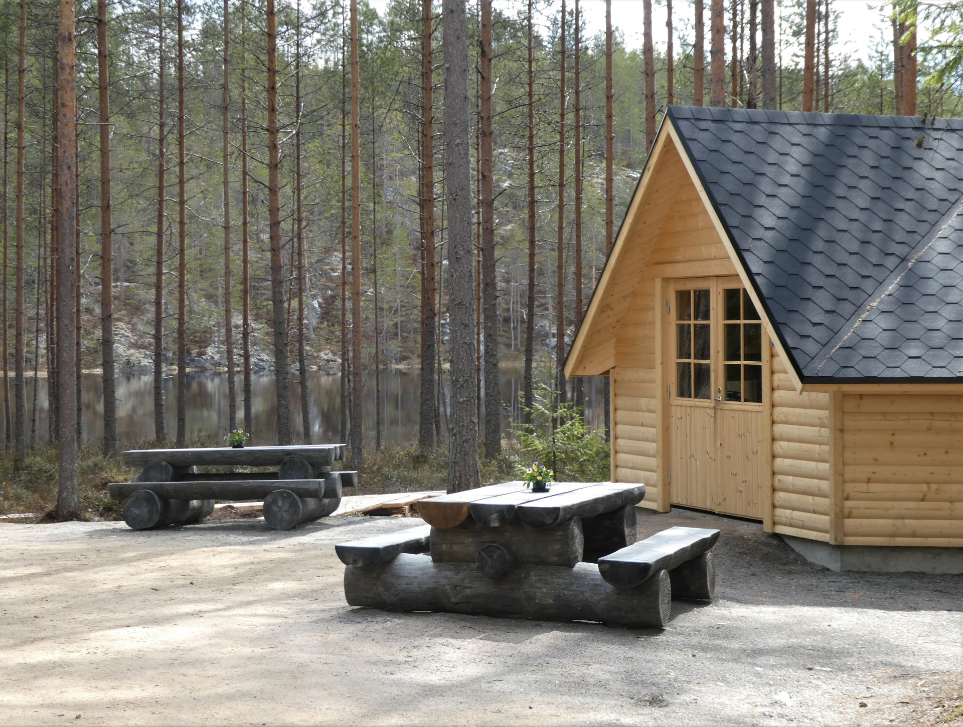 Seinävuoren rotkolaakso. Tuusniemi. Erittäin hyvin hoidetut vaellusreitit.
Puutarhamökki ja harjakattoinen puinen rakennus, edessä kivipöytä ja penkit, taustalla metsä ja järvi.