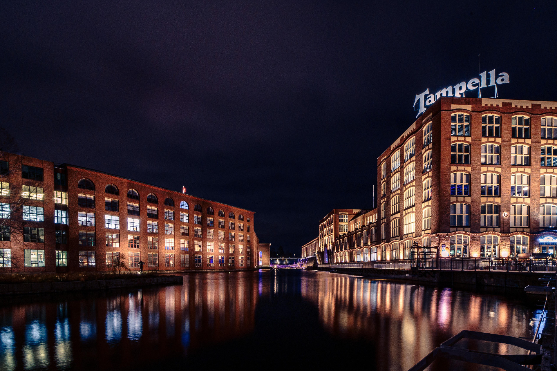 Tammerkoski ja Finlaysonin alue on Tampereen sydän.
Yönyöinen kanavanäkymä tiilirakennuksista, valaistut ikkunat ja heijastukset vedessä, taustalla “Tampella” -teksti.