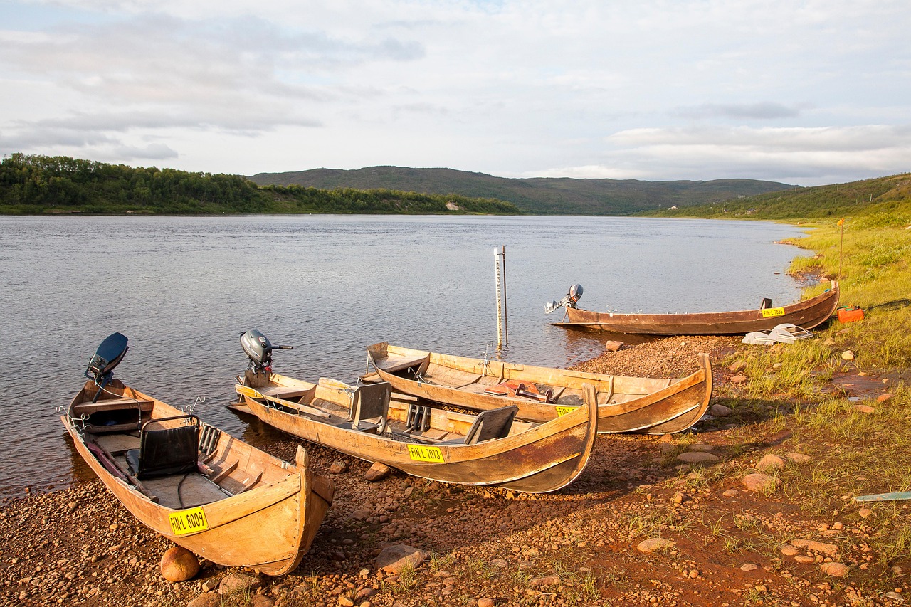 Lohen kalastus Simossa - Mertakoski, Kiusankoski, Merikoski, Saukkokoski ja muut Simojoen kalastuskohteet.
Puiset kalastusveneet rannassa järven rannalla, tyyni vesi ja mäkinen maisema taustalla.