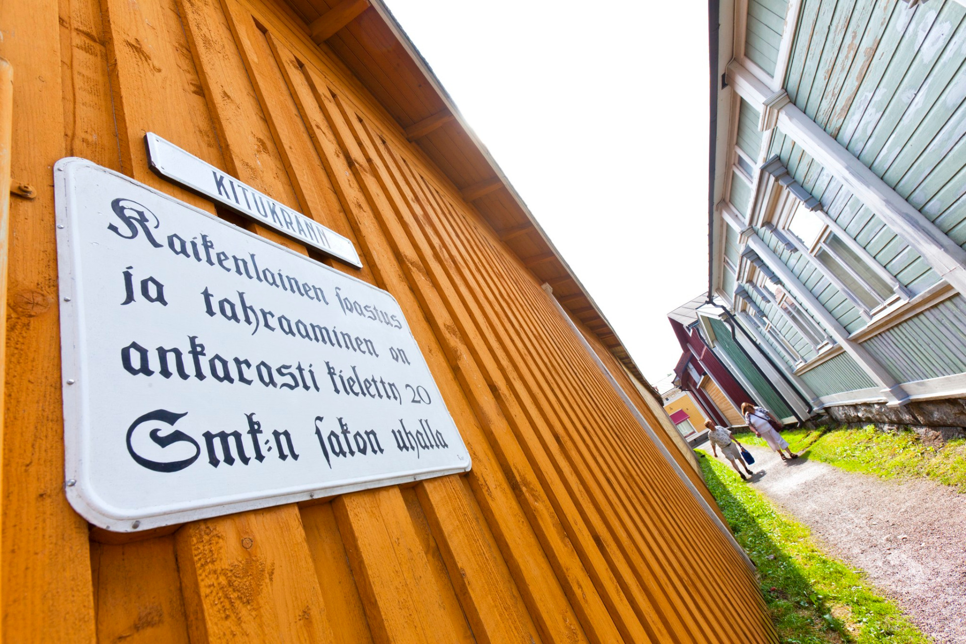 Kitukränn on kapea katu Vanhassa Raumassa. 
Keltainen puutalo, kyltti saksalaisella tekstillä ja sinivihreä veranta, taustalla nurmikko ja kulkijoita.