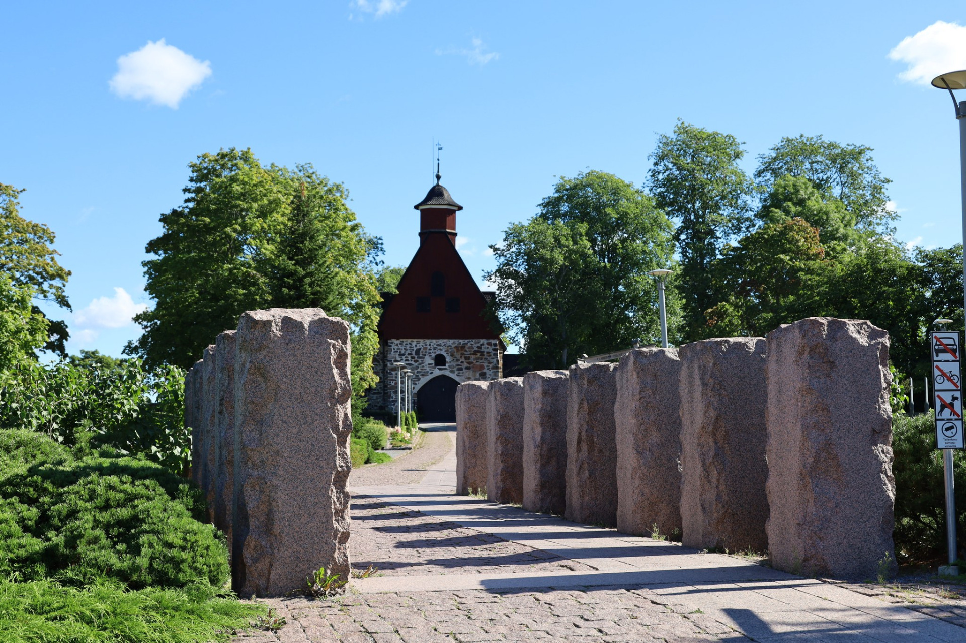 Raision keskiaikainen kivikirkko Varsinais-Suomessa
Kivinen käytävä ja punatiilinen kappeli, jonka tornissa on musta katto, ympärillä vehreää puistoa.