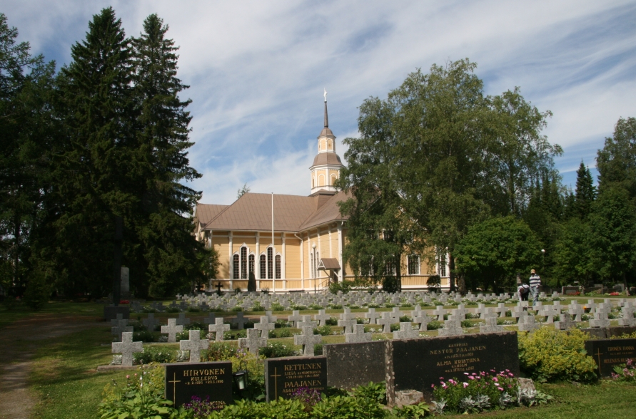 Pyhäjärven kaupungin kirkko on valmistunut vuonna 1897
Kirkko ja hautausmaa risteineen, ympärillä mäntyjä ja koivuja, taustalla pilvinen taivas.