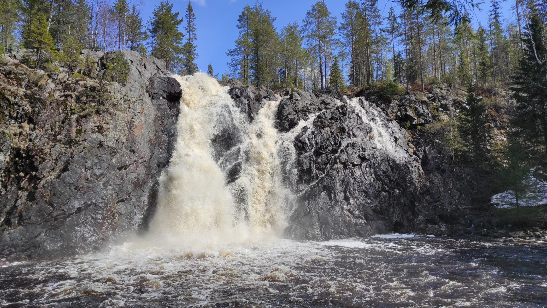 Hepokönkään vesiputous Puolangalla on hyvä retkikohde.
Vesiputous syöksyy kiviseen rotkoon, vaahtoa ja sumua, ympärillä havumetsä ja sininen taivas.
