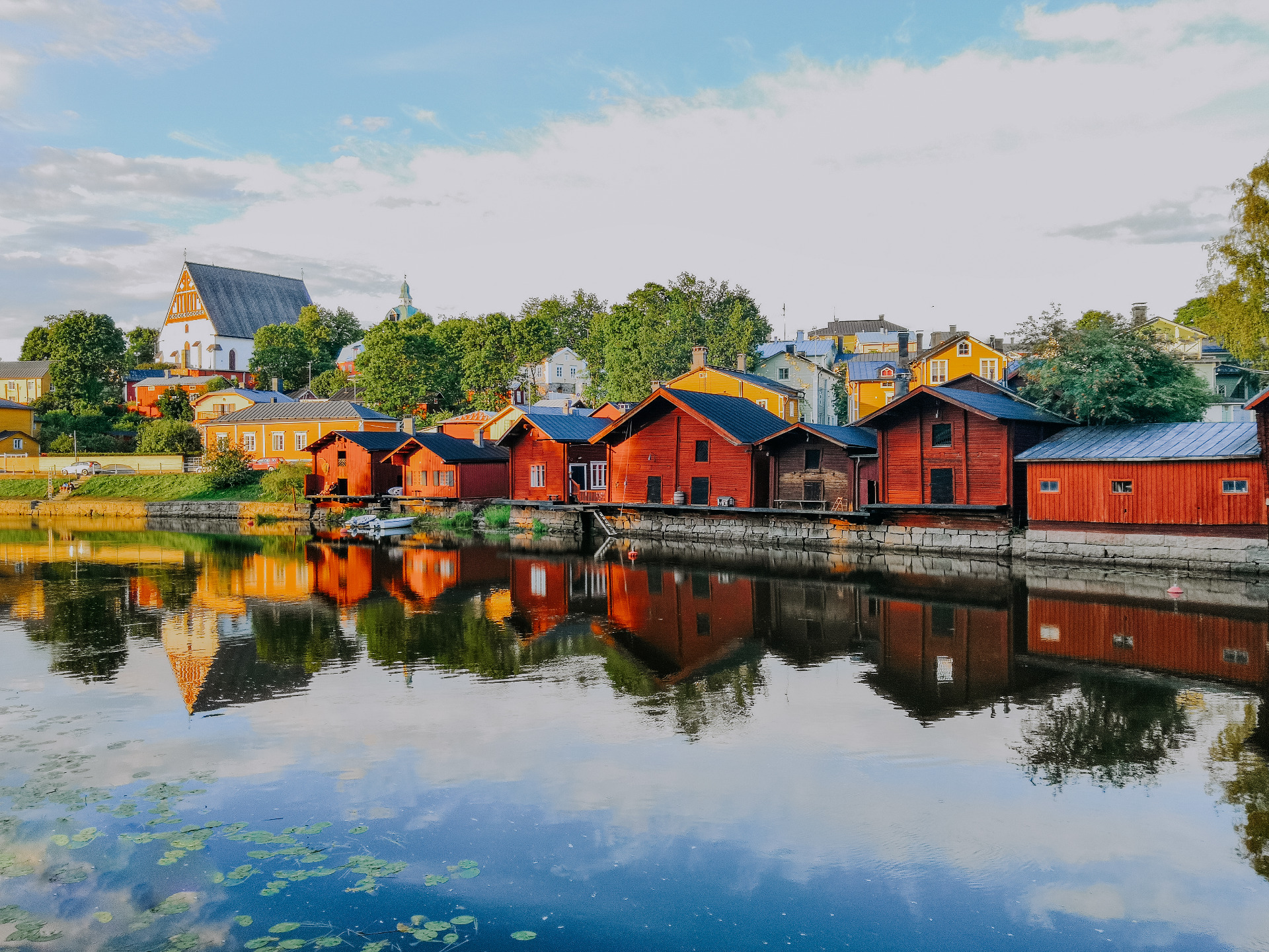 Porvoo on idyllinen ja rauhallinen vierailukohde.
Punaisia puutaloja ja kirkko, heijastukset rauhallisessa järvessä, sininen taivas ja vehreää kasvillisuutta.