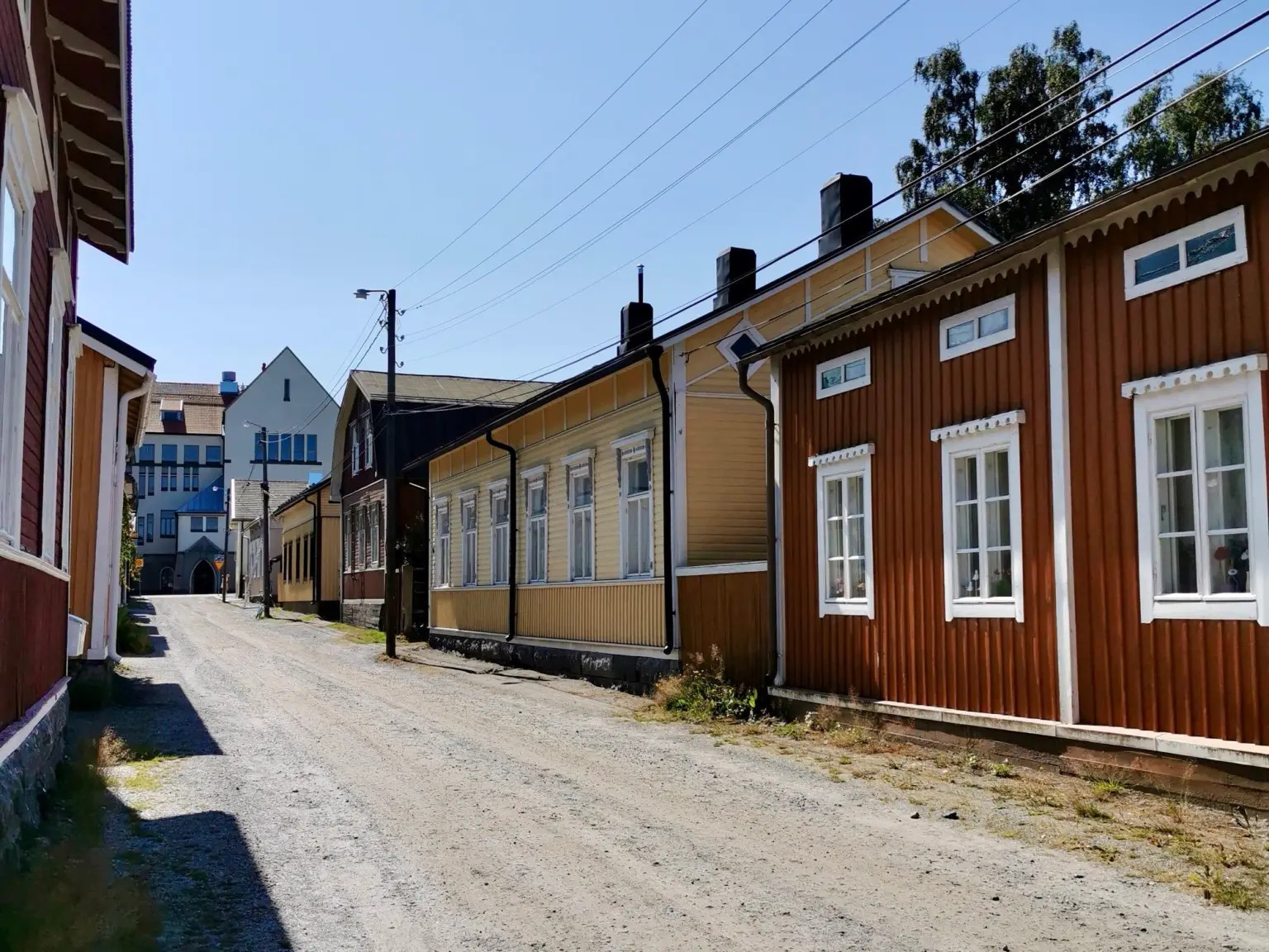 Skata on idyllinen puutaloalue Pietarsaaressa.
Kapea katu, rivitaloja ja puutaloja, punaisia ja keltaisia julkisivuja, ikkunat ja sähkölinjat taivaalla.