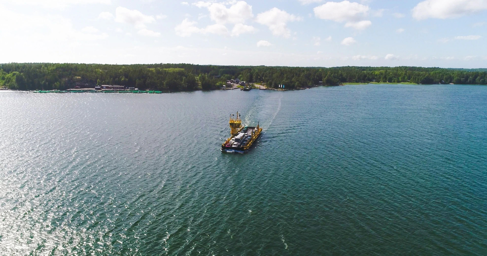 Paraisten ja saariston välillä kulkee lossiyhteys.
Keltainen lossi kulkee merellä, perässä valkoinen vaahtojälki, metsärannat ja pilvinen taivas taustalla.