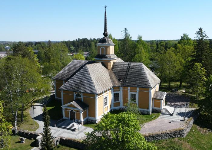 Nurmijärven kirkko Uudellamaalla.
Keltainen kirkko, harmaat kattotiilet ja kellotorni, ympärillä puisto ja nurmikko, ilmakuva.