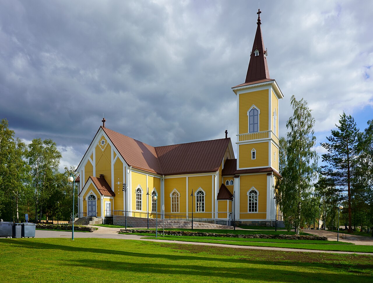 Nivalan kirkko on rakennettu 1803
Keltainen puukirkko, punakattoinen torni ja ristejä, nurmikkoa sekä puita pilvisellä taivaalla.