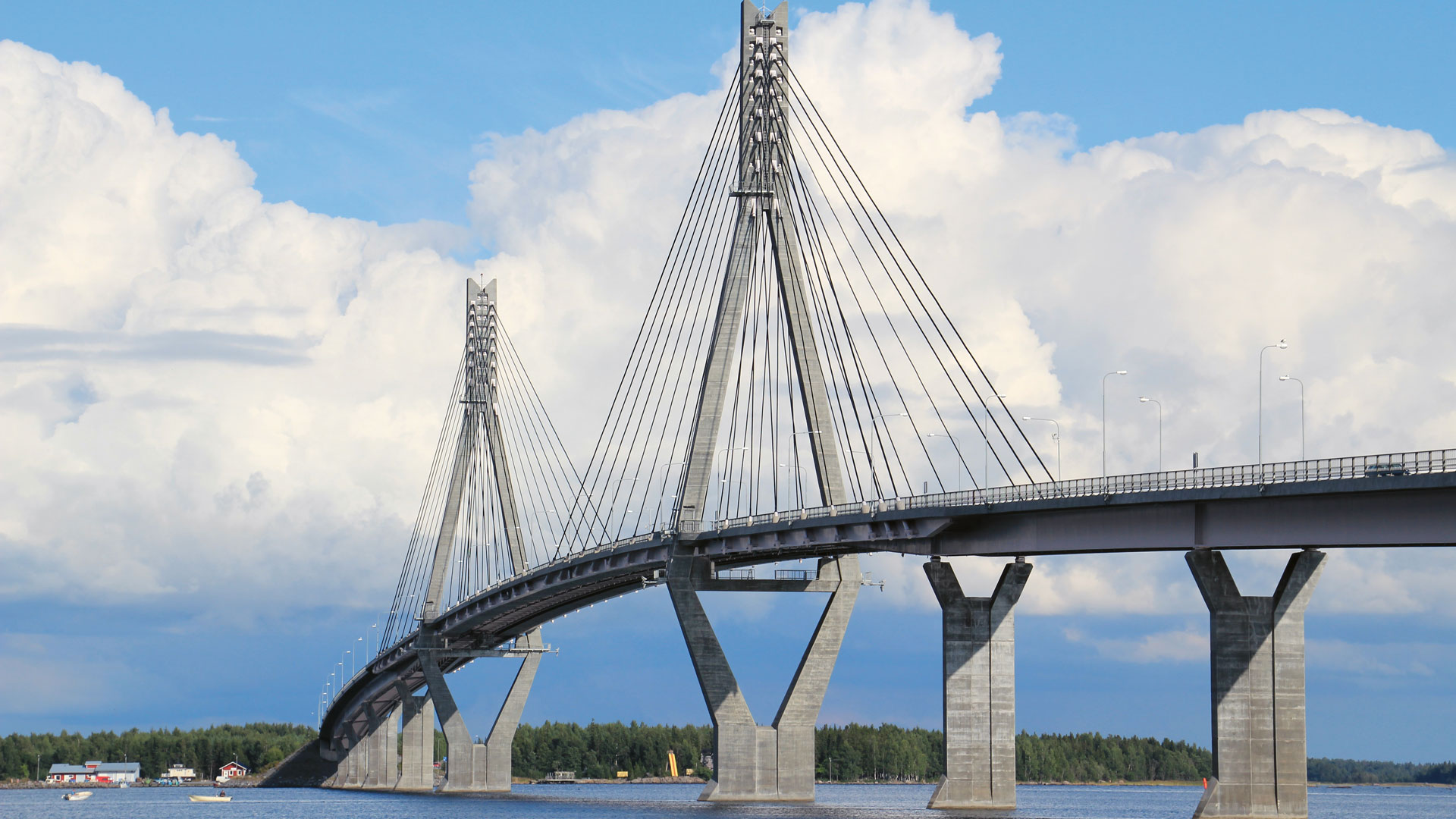 Raippaluodon silta Mustasaaressa, Pohjanmaalla.
Kaapelinen silta kohoaa taivaalle, teräspylväät ja vinot kaapelit näkyvät pilvien keskellä.
