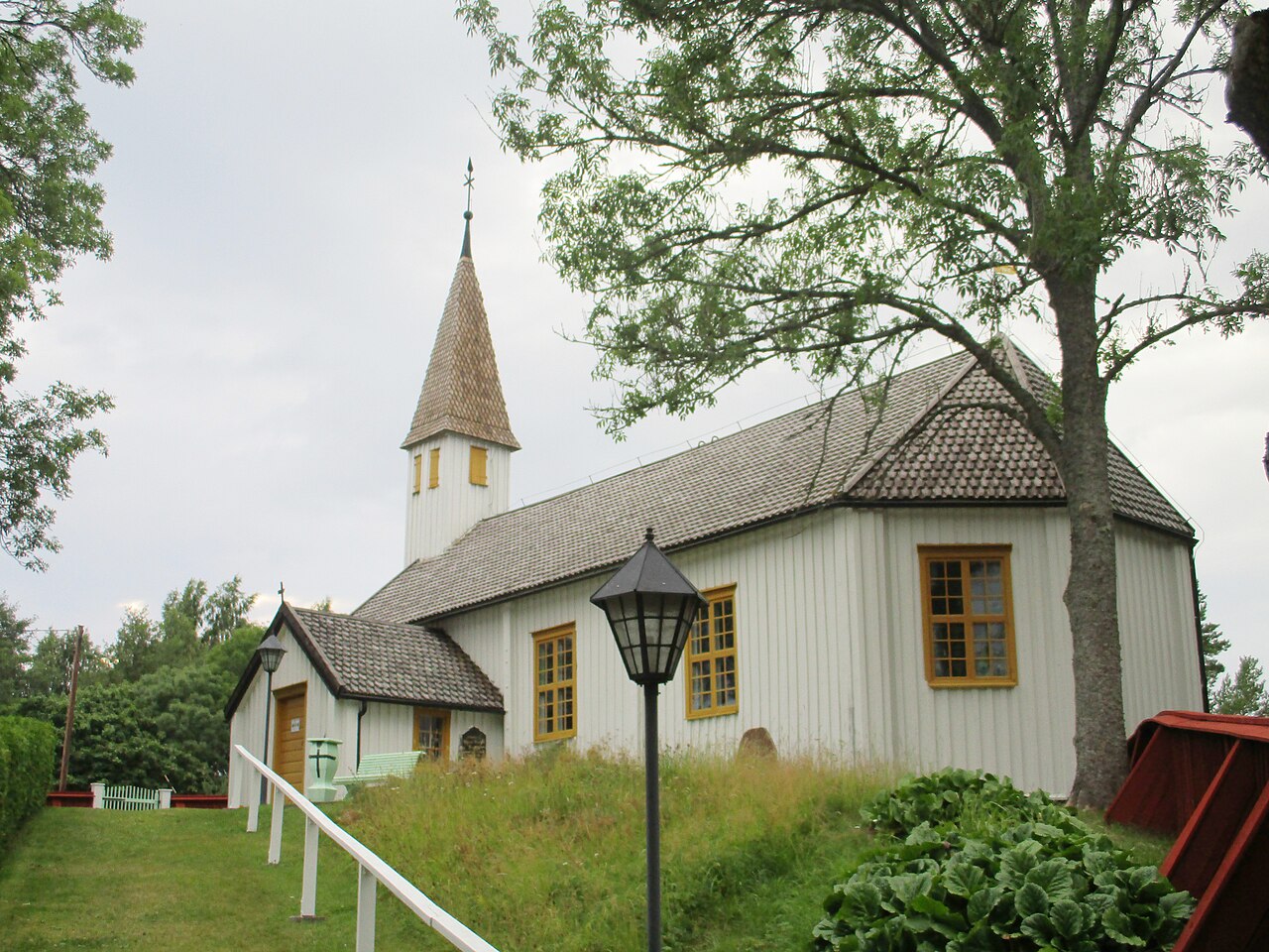 Lumparlandin kirkko on Ahvenanmaan vanhin säilynyt puukirkko.
Valkoinen puukirkko, harmaa katto ja torni, ympärillä ruohoa, pensaita ja puu.