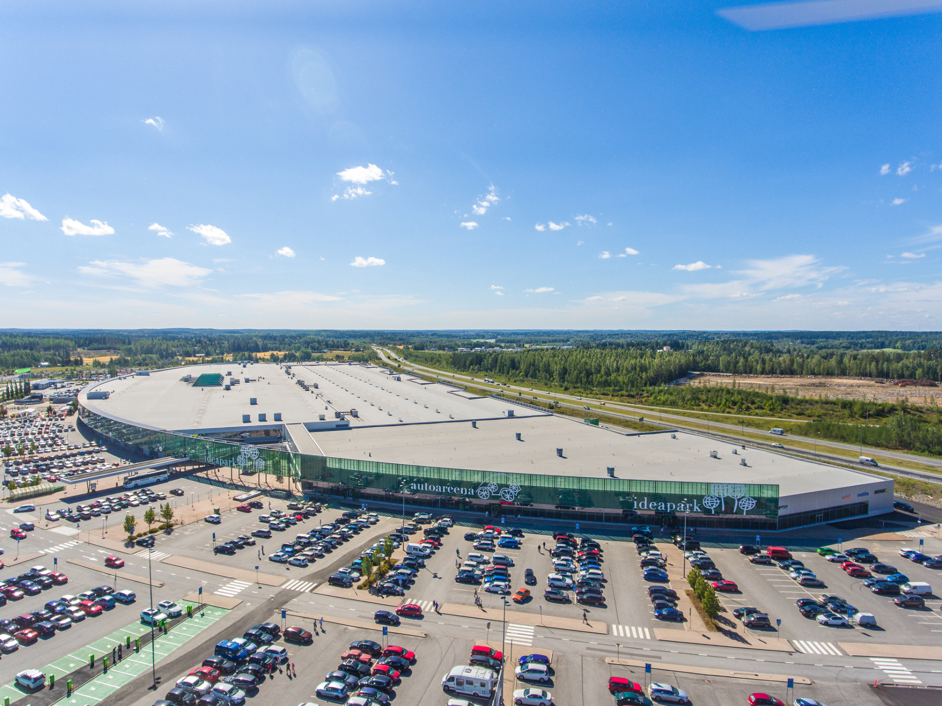 Lempäälän kunnan suosituin vierailukohde on kauppakeskus Ideapark.
Ilmakuva autopaikoitusalueesta ja Ideapark-ostoskeskuksesta, taustalla metsää ja sininen taivas pilvineen.
