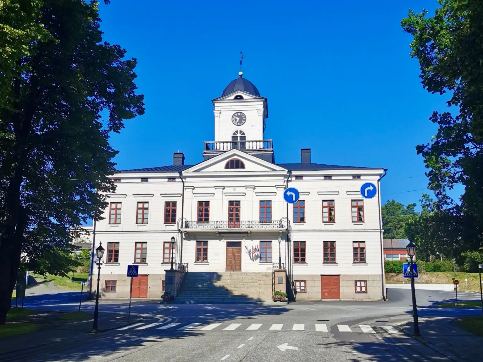 Vuonna 1856 valmistunut raatihuone on yksi Kristiinankaupungin tunnetuimmista rakennuksista. 
Valkoinen historiallinen rakennus kellotorneineen, sininen taivas ja puita ympärillä, edessä suojatie.