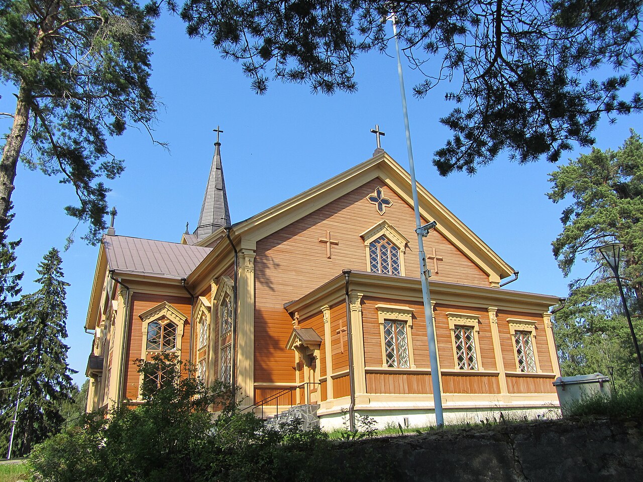 Kontiolahden kirkko valmistui vuonna 1881.
Keltainen puukirkko, risti-ikkunakoristeet ja kellotorni, ympärillä mäntyjä sinistä taivasta vasten.