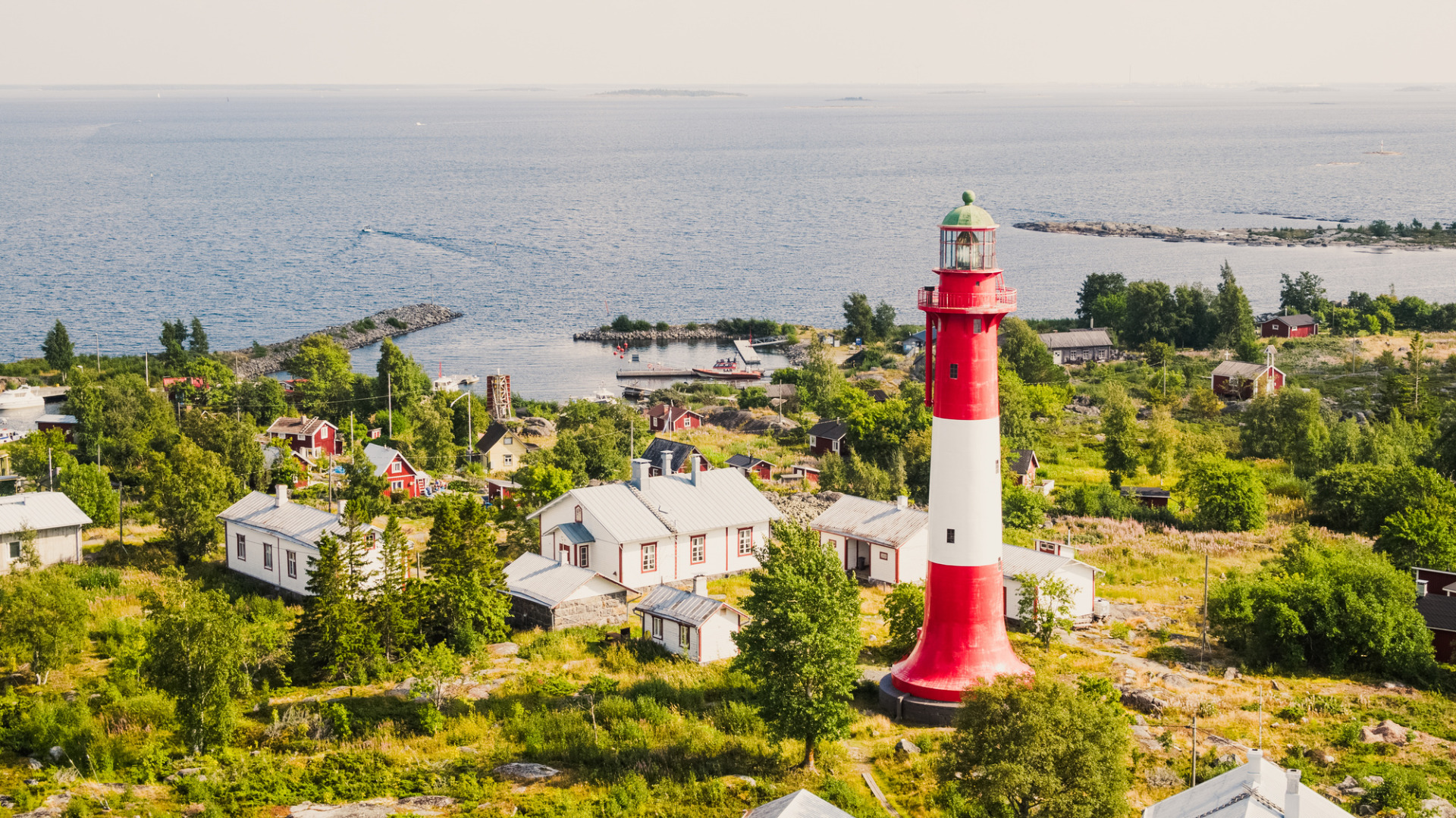 Tankarin majakka, Kokkola Keski-Pohjanmaalla.
Punavalkoinen majakka kohoaa rannikkokylän ylle, taustalla sininen meri ja kaukaista horisonttia.