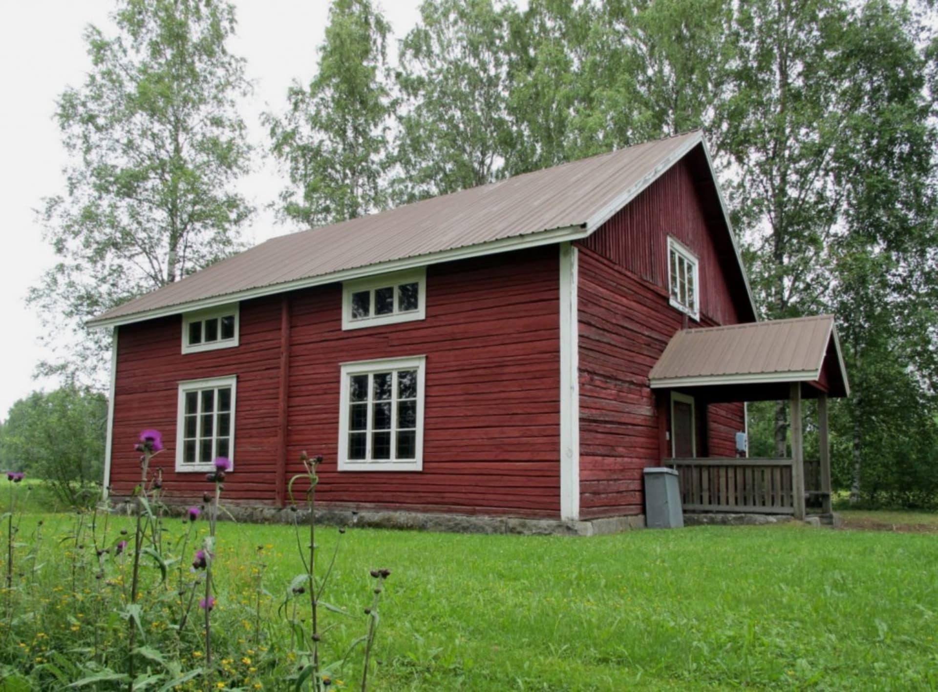 Kihniön Esinemuseo Pirkanmaalla.
Punainen hirsitalo, valkoiset ikkunanpuitteet ja katettu kuisti, ympärillä vihreä nurmikko ja puut.